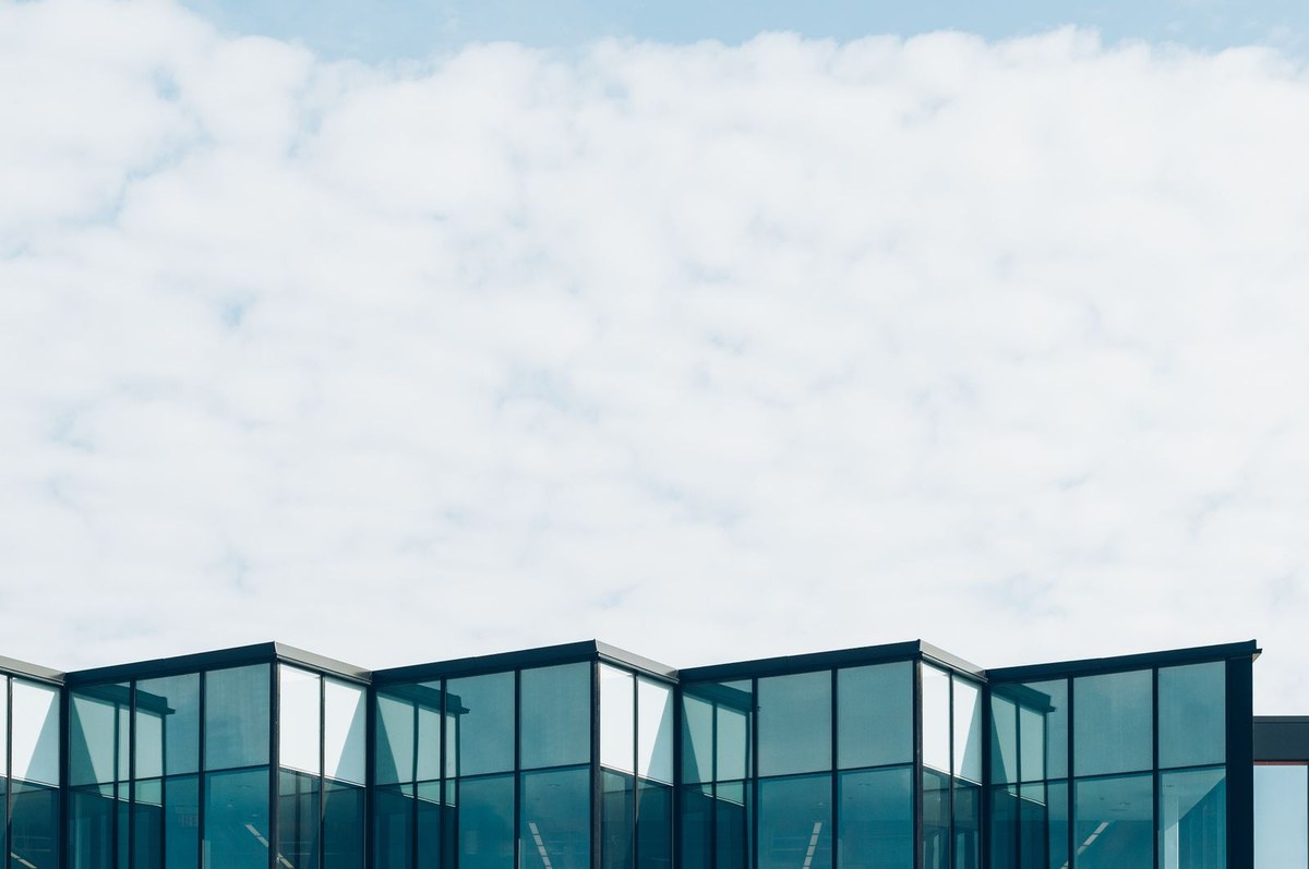 Modern geometric glass commercial facade with a sawtooth roofline against cloudy sky